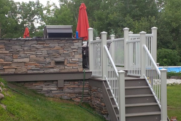 custom deck with stone walls and stairs with railings leading to backyard grass